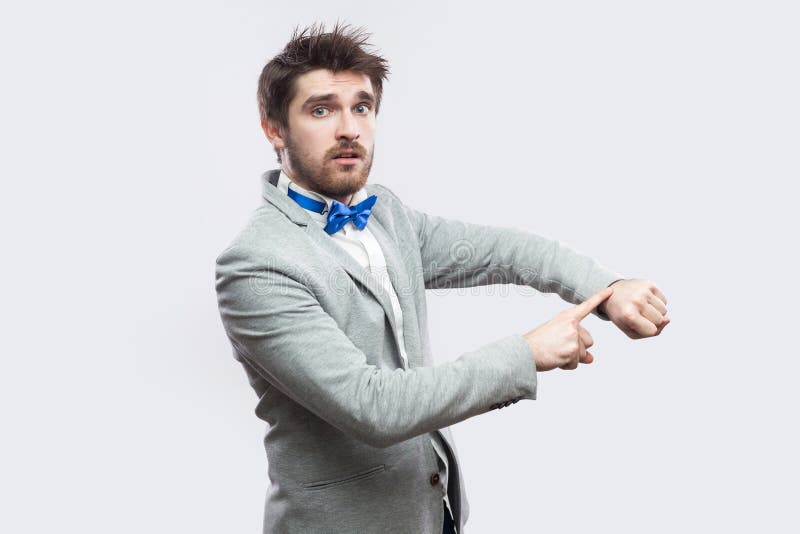 Portrait of serious worried handsome bearded man in casual grey suit and blue bow tie standing with watch hand gesture and looking royalty free stock photos Portrait of serious worried handsome bearded man in casual grey suit and blue bow tie standing with watch hand gesture and looking royalty free stock photos