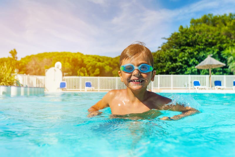 Boy with swimming goggles standing in outdoor pool