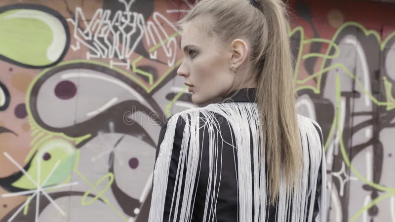 A portrait of a sexy brown haired girl with a ponytail wearing stylish black jacket with white long fringe standing