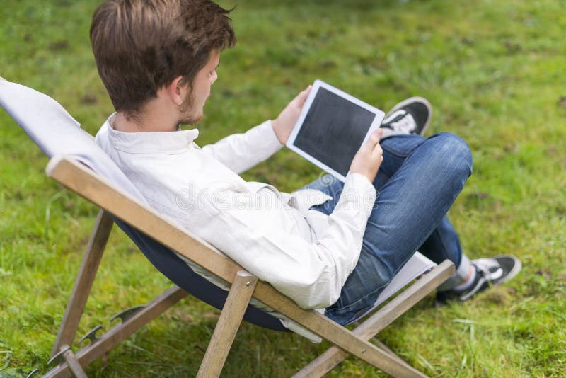 Portrait of sitting young man on grass with digital tablet