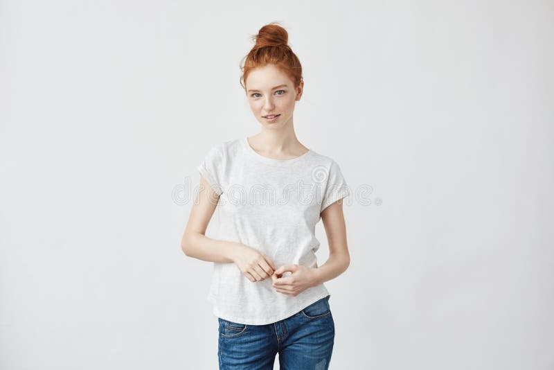 Portrait of smart redhead girl flirting on camera feeling insecure yet to meet her boyfriend. Weating jeans and a bun, lifestyle concept on white. copy space.