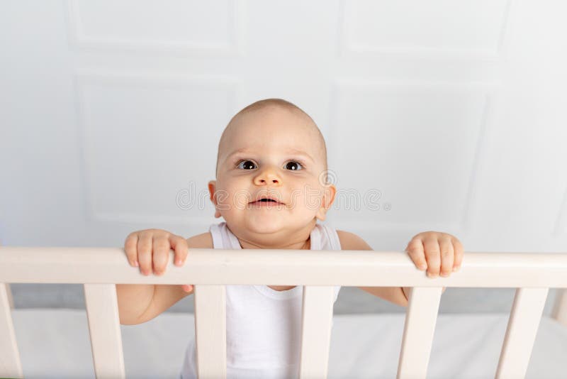 Portrait Of A Smiling Baby Boy 8 Months Old Standing In A Crib In A