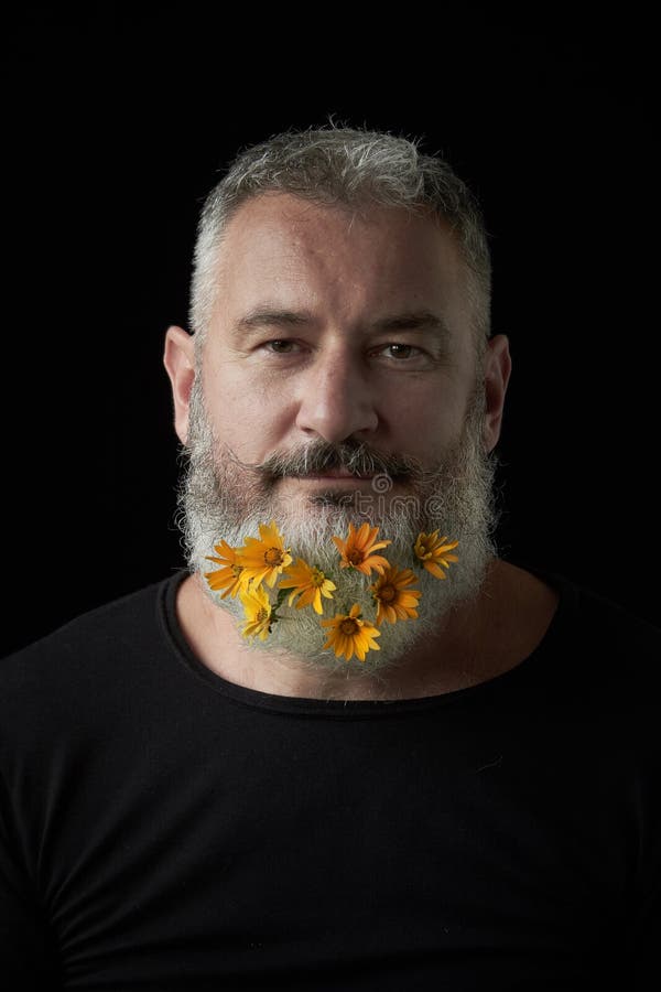 Portrait of a smiling brutal man with a gray beard decorated with yellow flowers on a black background, selective focus royalty free stock images Portrait of a smiling brutal man with a gray beard decorated with yellow flowers on a black background, selective focus royalty free stock images