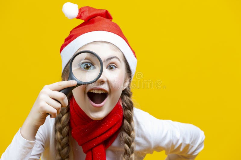 Portrait of Smiling Caucasian Girl in Santa Hat Holding Empty Big Magnifying Glass While Searching and Posing on Viewer