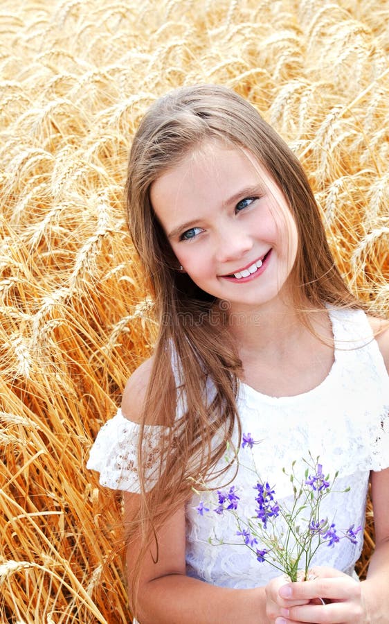 Portrait of smiling cute little girl child on field of wheat holding flowers