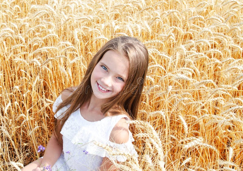 Portrait of smiling cute little girl child on field of wheat holding flowers