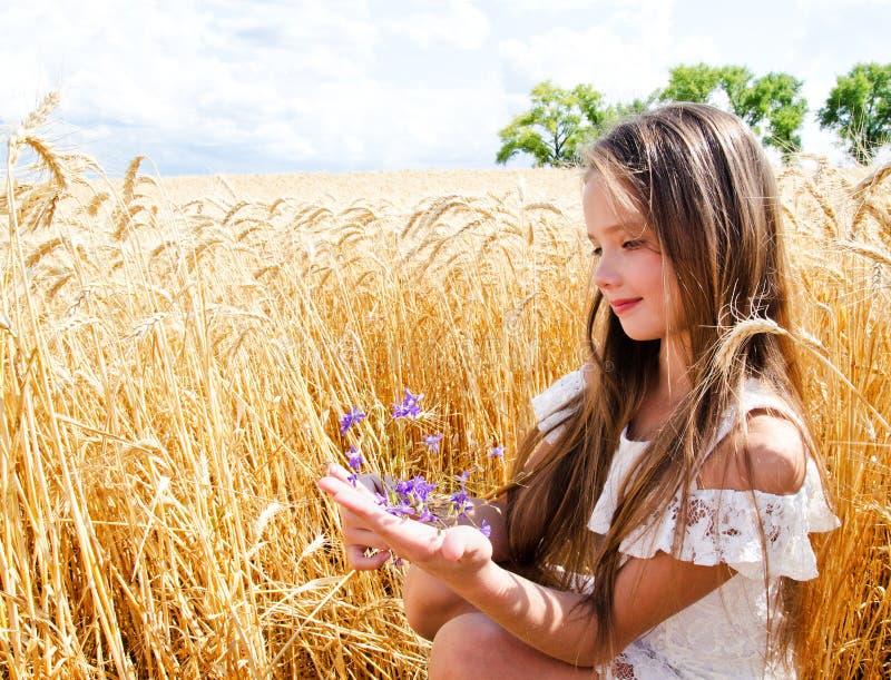 Portrait of smiling cute little girl child on field of wheat holding flowers