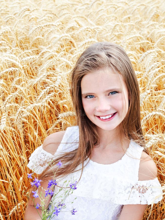 Portrait of smiling cute little girl child on field of wheat holding flowers