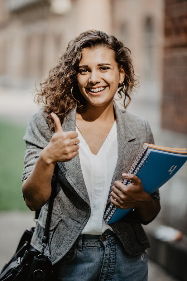 Portrait Of A Smiling Female Student Showing Thumb Up Outdoors Stock