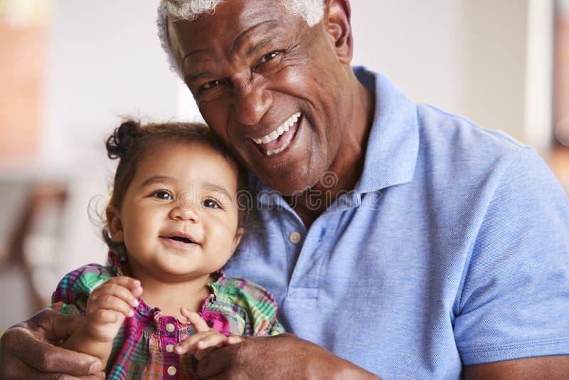 Portrait Of Smiling Grandfather Sitting On Sofa At Home With Baby Granddaughter stock photos