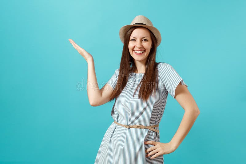 Portrait of smiling happy young elegant woman wearing dress, straw summer hat pointing hand aside on copy space isolated