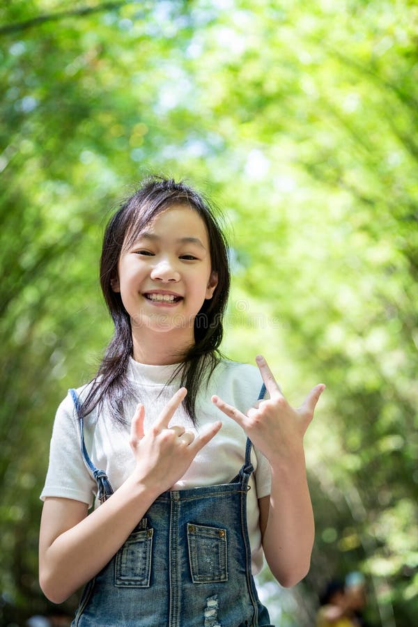 Portrait of smiling little asian girl right sign language meaning I Love You and look at the camera on bamboo forest,green nature stock photography Portrait of smiling little asian girl right sign language meaning I Love You and look at the camera on bamboo forest,green nature stock photography