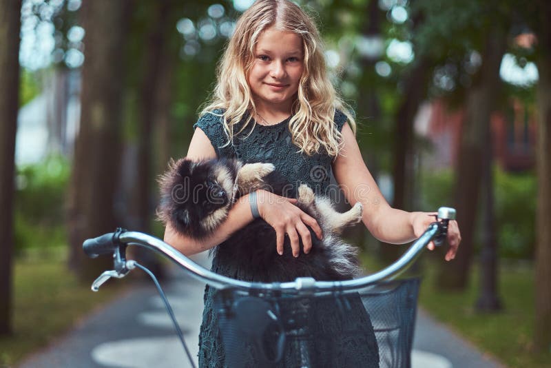 Portrait Of A Little Blonde Girl In A Casual Dress Holds Cute Spitz