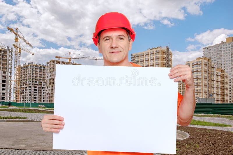 Portrait smiling middle-aged handsome worker wearing red hard hat, looking to the camera and holding blank paper sheet stock image Portrait smiling middle-aged handsome worker wearing red hard hat, looking to the camera and holding blank paper sheet stock image