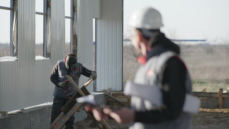 Smiling professional engineer in protective uniform wearing safety glasses and helmet background of a welder and welding stock footage