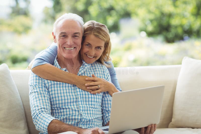 Portrait of smiling senior woman embracing a man in living room while using laptop royalty free stock photography Portrait of smiling senior woman embracing a man in living room while using laptop royalty free stock photography