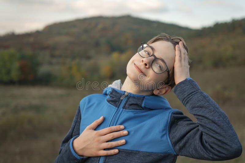 Portrait of smiling teenage boy with glasses on mountain landscape background. Child on walk in nature in autumn