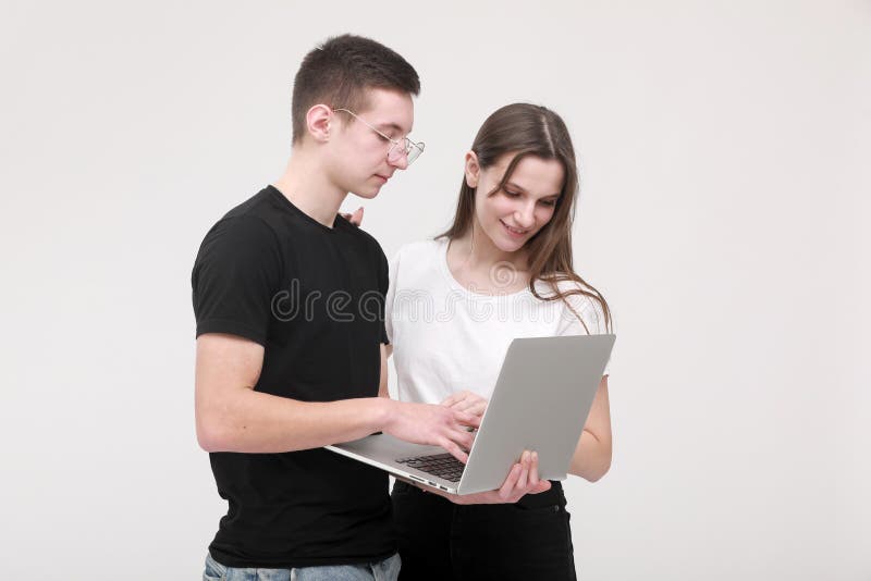 Portrait of a smiling teens boy and girl holding laptop computer while standing and looking in it isolated over white