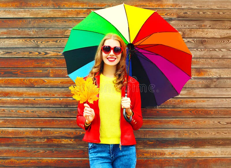 Portrait smiling woman with colorful umbrella in autumn with maple leaves over wooden background