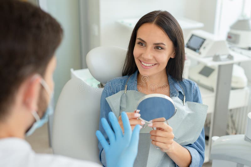 Portrait of smiling woman holding mirror and talking with dentist