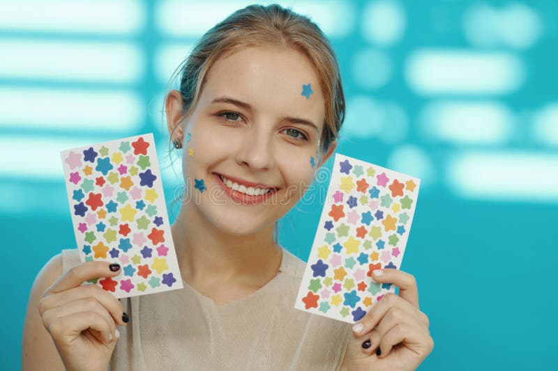 Portrait of Smiling Woman Holding Star Patterned Sheets. Portrait of woman smiling while holding two sheets with colorful star patterns against a blurred background, with blue star stickers on her face and shoulders