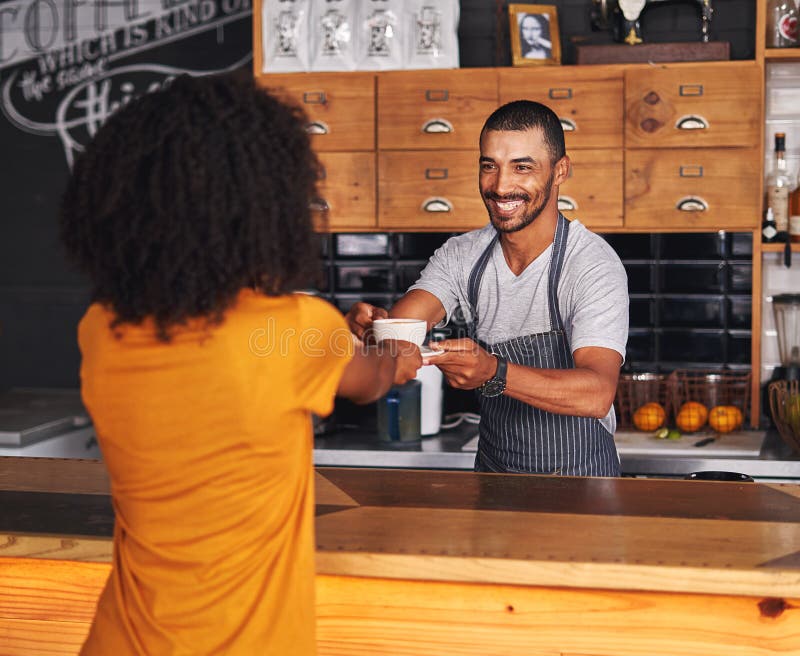 Portrait of a smiling young coffee shop owner in apron handing over a coffee cup to female customer. Portrait of a smiling young coffee shop owner in apron handing over a coffee cup to female customer