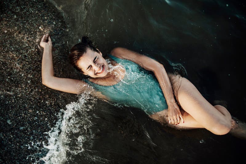 Portrait of smiling young woman in swimsuit splashing a wave