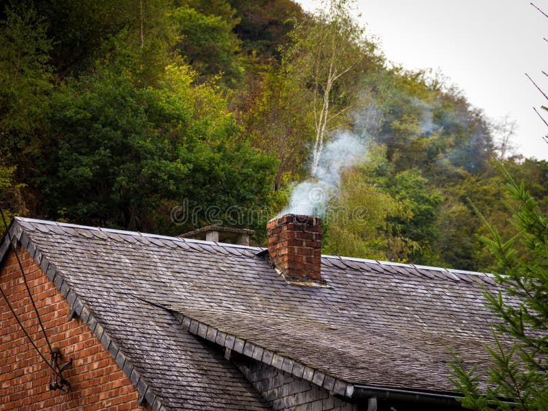 A portrait of a smoking chimney from a fire place inside an old house on a roof. You can see how polluting the smoke is from