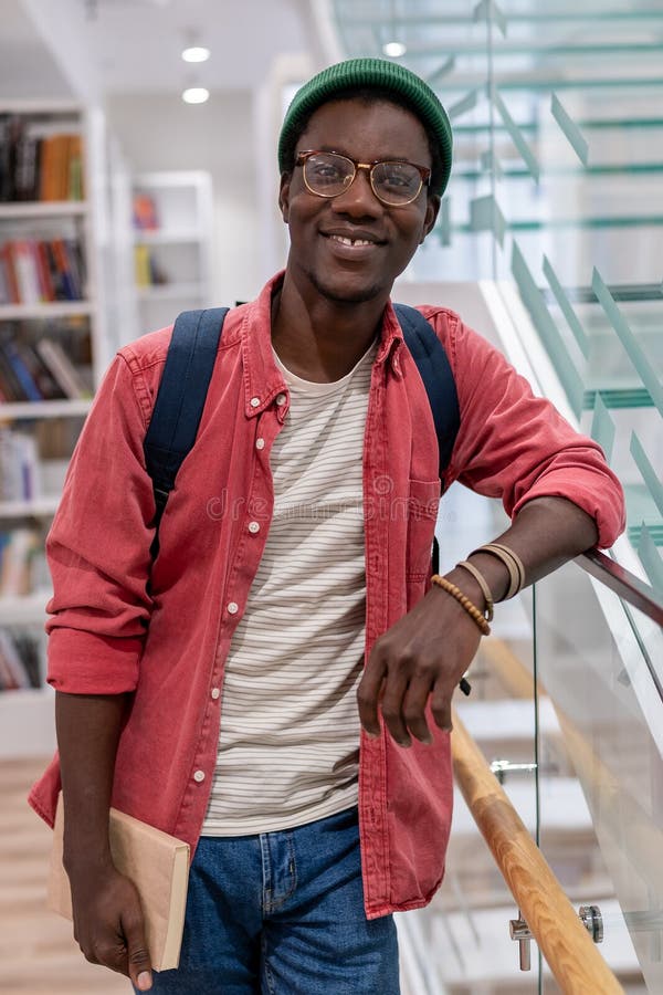 Portrait sourire heureux afro-américain étudiant hipster gars avec des livres dans la bibliothèque universitaire du campus image libre de droits