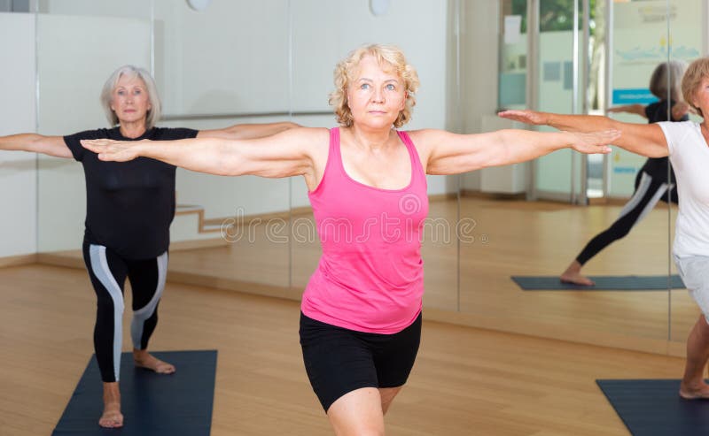 Portrait of sporty mature woman practicing Virabhadrasana known as Warrior Pose during group yoga training. Portrait of sporty mature woman practicing Virabhadrasana known as Warrior Pose during group yoga training.