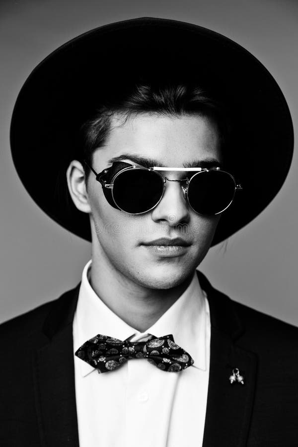 Portrait of a stylish young man in hat wearing elegant suit and sunglasses.