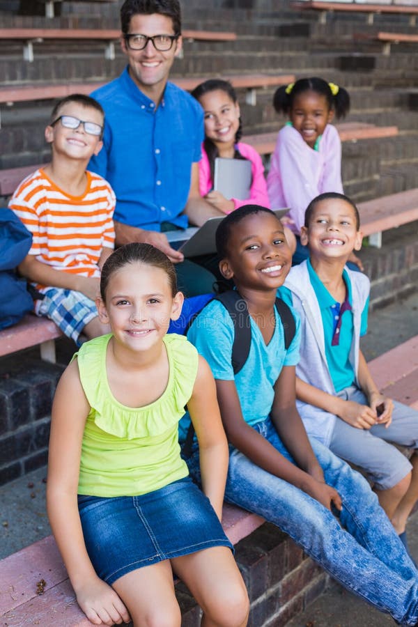 Portrait of smiling teacher and kids sitting on bench at school. Portrait of smiling teacher and kids sitting on bench at school