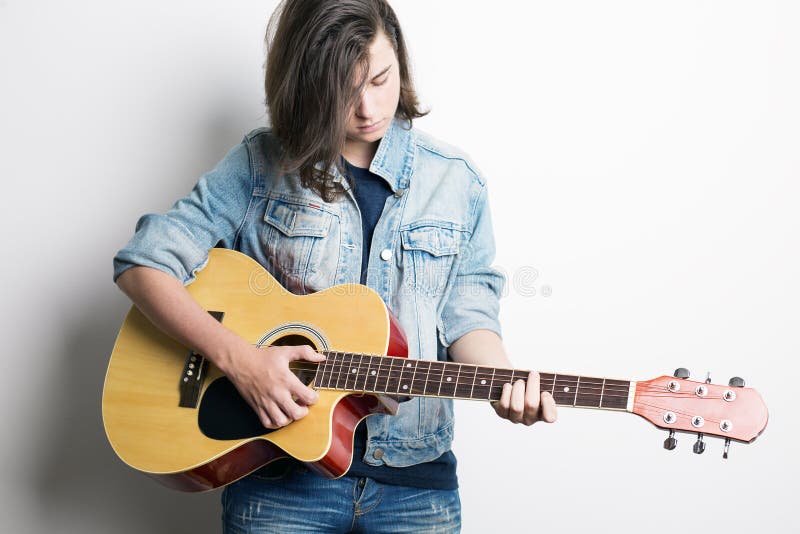 Fashion portrait of a teenager playing guitar in studio wearing jeans jacket