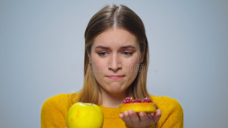 Portrait of thoughtful woman selecting between apple or cake at camera.