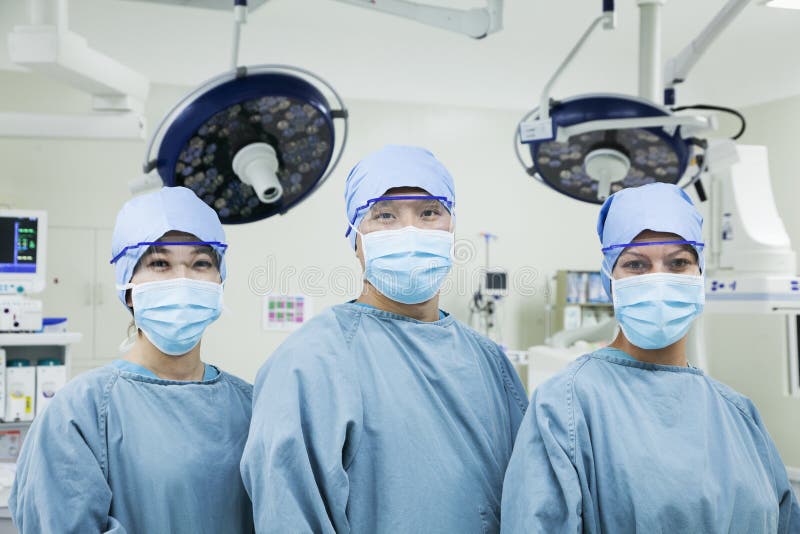 Portrait of three surgeons in a row wearing surgical masks in the operating room, looking at camera stock images