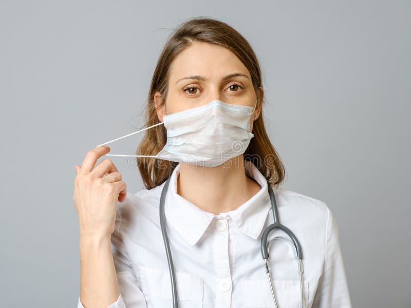 Portrait of tired young doctor taking off medical face mask