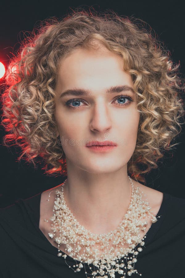 portrait of transgender guy model with blue eyes and blond hair in the image of a girl with beads around neck