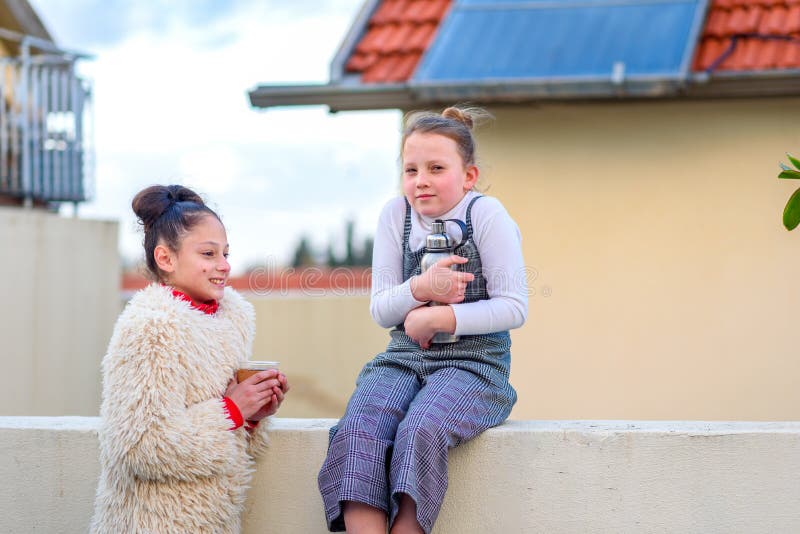 Two happy girls feeling cold outdoor in the city. Young teenagers with reusable bottle and cup on a roof. stock photos Two happy girls feeling cold outdoor in the city. Young teenagers with reusable bottle and cup on a roof. stock photos