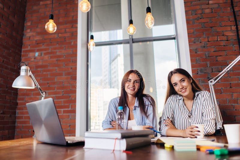 Portrait of two female students smiling, sitting at desk, looking at camera preparing for lessons, doing homework stock photos Portrait of two female students smiling, sitting at desk, looking at camera preparing for lessons, doing homework stock photos
