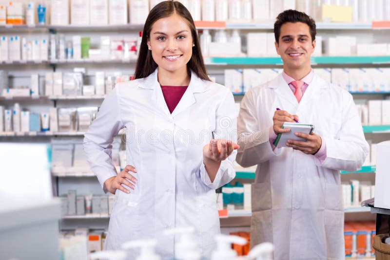 Portrait of two cheerful friendly pharmacists working in modern farmacy. Focus on the woman. Portrait of two cheerful friendly pharmacists working in modern farmacy. Focus on the woman