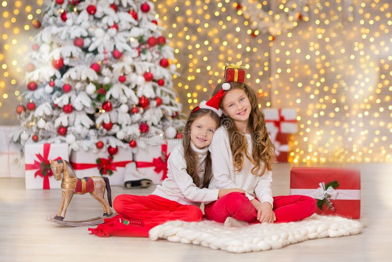 Portrait of two one young girls sisters close to white green Christmas tree. The girls in beautiful evening dresses clothes in New