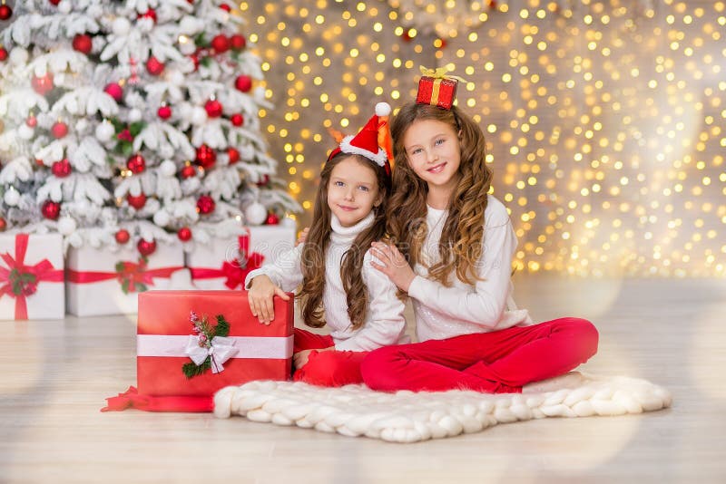 Portrait of two one young girls sisters close to white green Christmas tree. The girls in beautiful evening dresses clothes in New