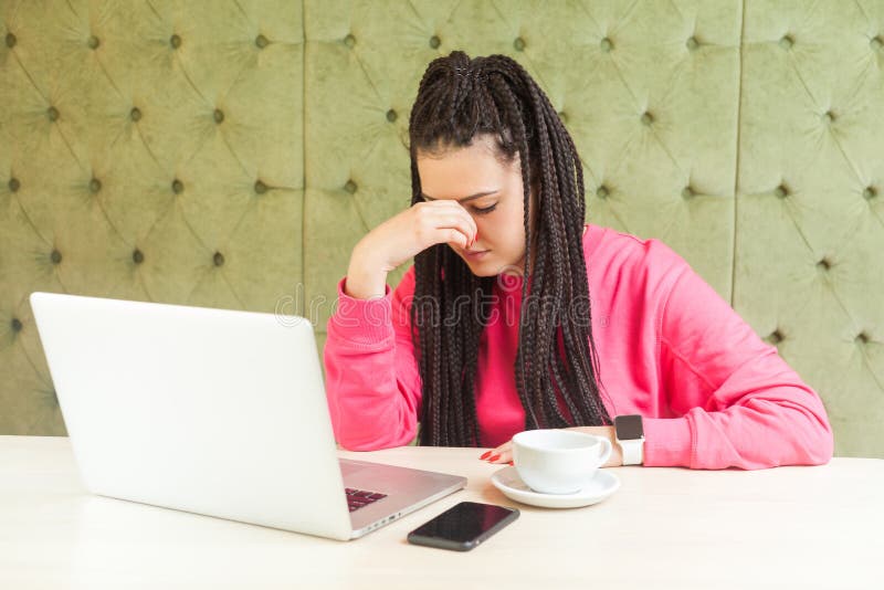 Portrait of unhappy young girl freelancer with black dreadlocks hairstyle in pink blouse sitting and working on laptop, closed stock photos Portrait of unhappy young girl freelancer with black dreadlocks hairstyle in pink blouse sitting and working on laptop, closed stock photos