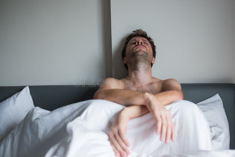 Portrait of an upset young man sitting on a bed alone. He break up with his girlfriend and now is missing her