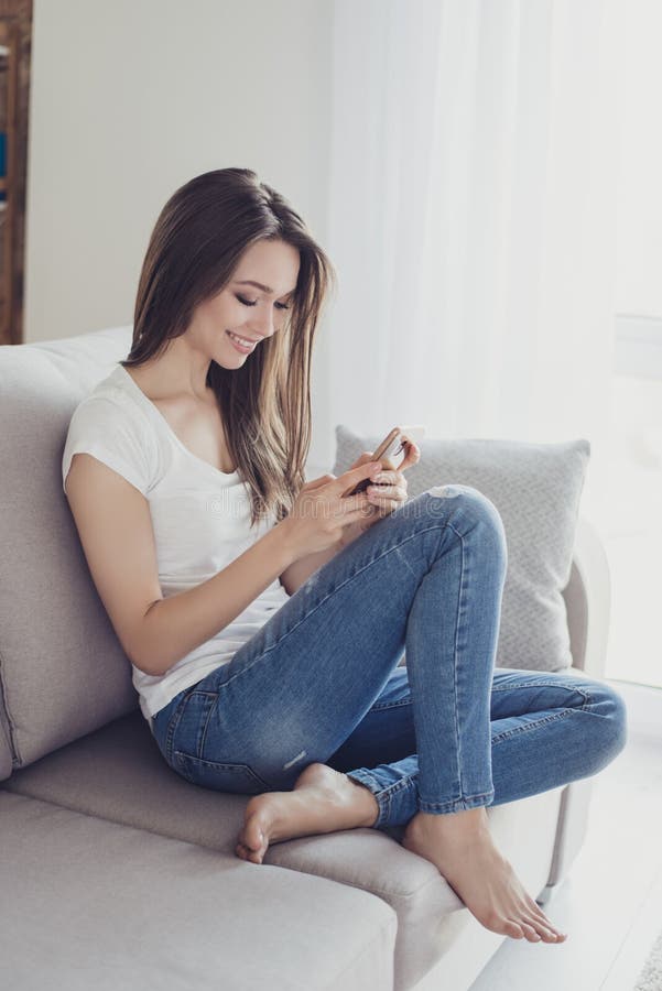 Portrait vertical de la fille assez heureuse de jeunes s'asseyant sur l'usi de sofa photographie stock Portrait vertical de la fille assez heureuse de jeunes s'asseyant sur l'usi de sofa photographie stock