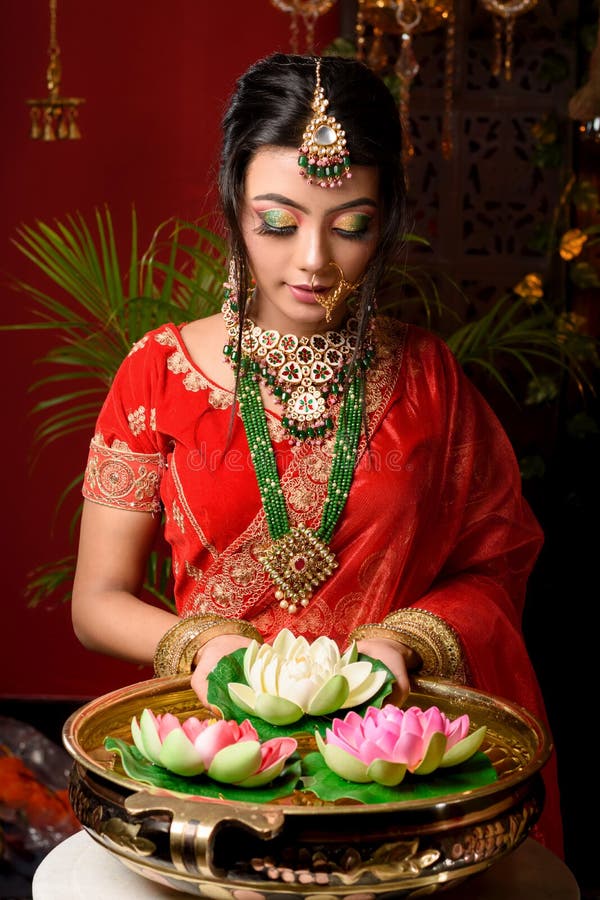 Portrait of very beautiful young Indian bride in luxurious bridal costume with makeup and heavy jewellery holding a lotus in