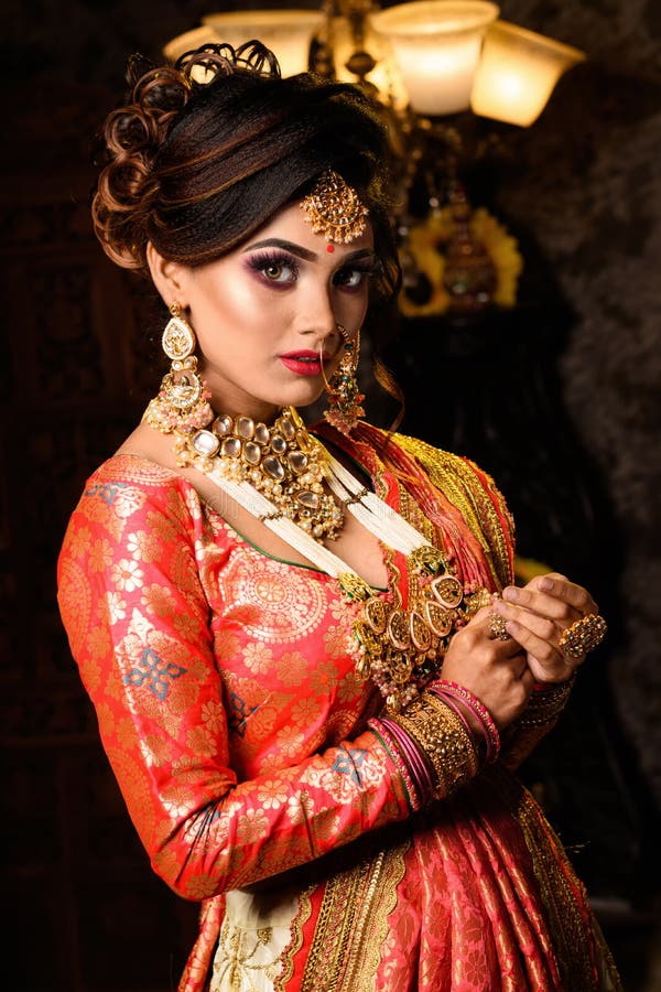 Portrait of very beautiful young Indian bride in luxurious bridal costume with makeup and heavy jewellery in studio lighting