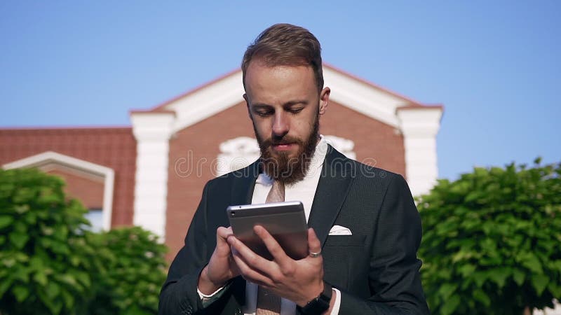 Portrait von Geschäftsmann in Anzug mit Krawatte mit Computertablette beim Spaziergang in der Nähe des Bürogebäudes