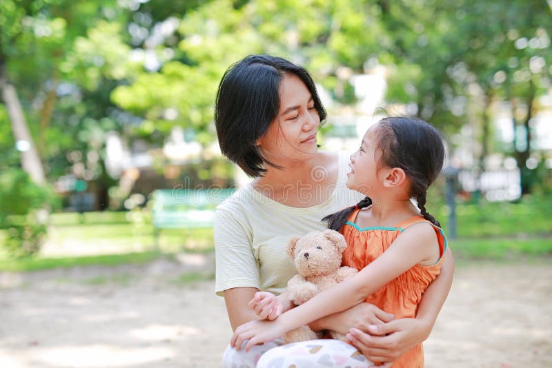 Portrait von glücklicher asiatischer Mutter-Kuscheltochter und umarmter Teddybären-Puppe im Garten Mutter und Kind mit Liebe und