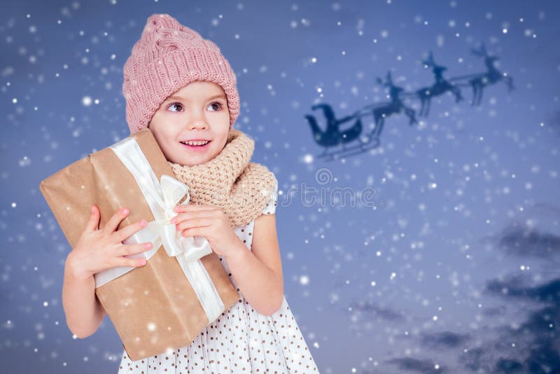 Portrait von kleinen Mädchen mit Geschenk in einem gestrickten Hut auf dunkelblauem Hintergrund Cute blonde Kind mit Weihnachtsge stockbilder Portrait von kleinen Mädchen mit Geschenk in einem gestrickten Hut auf dunkelblauem Hintergrund Cute blonde Kind mit Weihnachtsge stockbilder